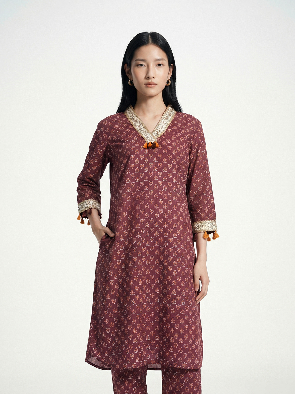 Female model wearing VUNN Kaashi Kurta — deep maroon hand-block printed cotton kurta with ochre florals, ivory gota-lace V-neck, tassel-trimmed sleeves and matching printed pants
