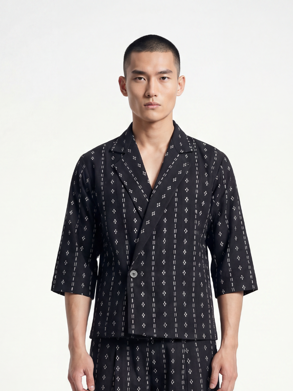 Male model wearing VUNN Black Woven Wrap Shirt — black hand-woven short-sleeve wrap shirt with ivory diamond motifs in vertical stripes, Cuban collar and matching woven trousers