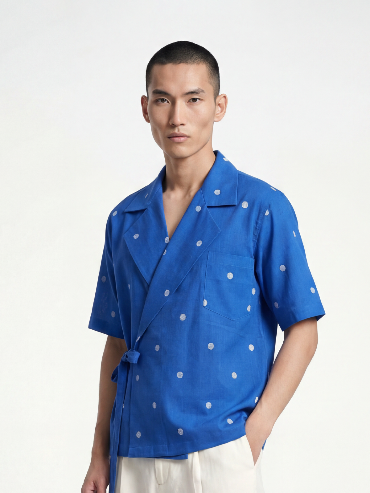 Male model wearing VUNN Indigo Dot Wrap Shirt — cobalt blue hand-loomed short-sleeve wrap shirt with cream buta dots, Cuban collar and side-tie closure
