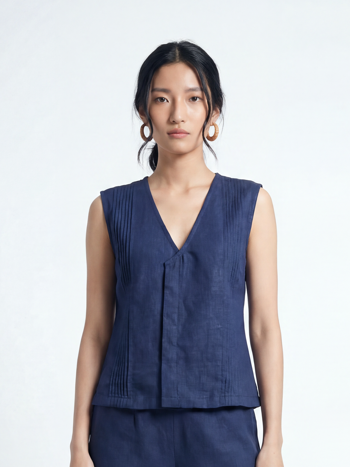 Female model wearing VUNN Indigo Pintuck Linen Top — deep indigo sleeveless linen top with a V-neckline and fine vertical pintuck detailing
