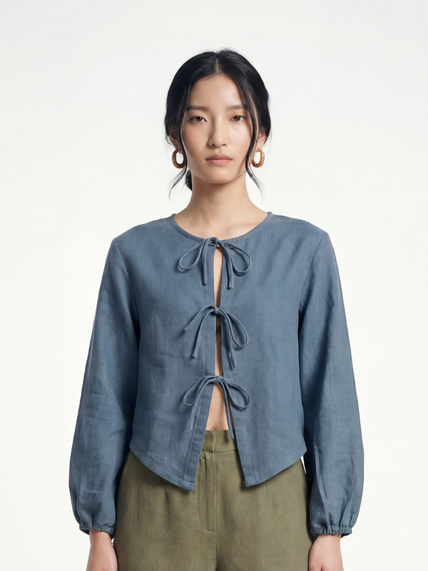 Female model wearing VUNN Steel Linen Tie-Front Top — steel-blue cropped linen top with a three-tie front closure and long balloon sleeves