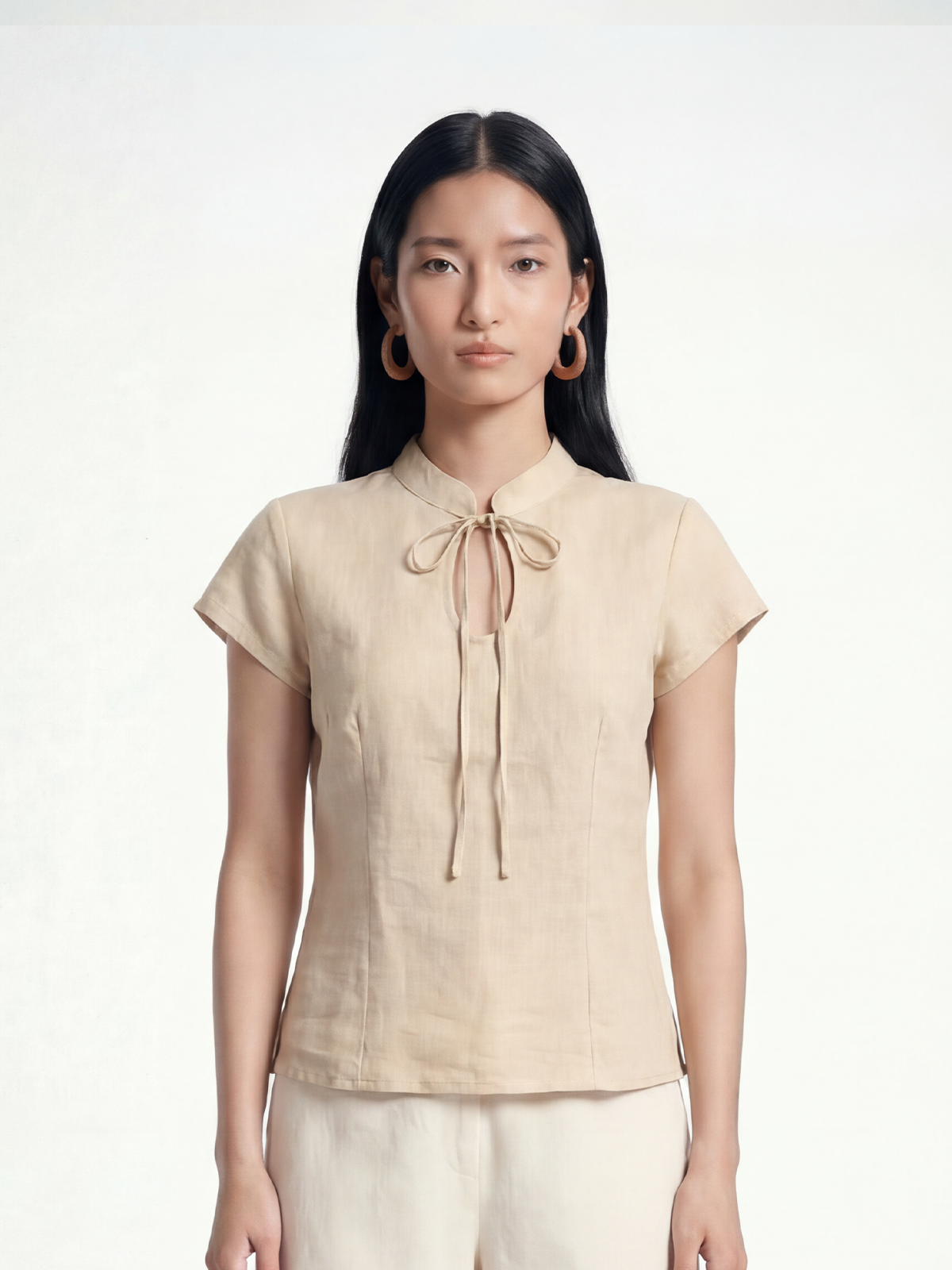 Female model wearing VUNN Oat Linen Tie-Neck Top — oat-coloured fitted linen top with a mandarin collar, slim neck-tie and short cap sleeves