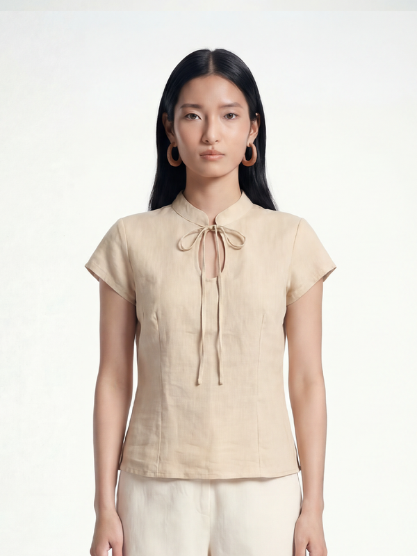 Female model wearing VUNN Oat Linen Tie-Neck Top — oat-coloured fitted linen top with a mandarin collar, slim neck-tie and short cap sleeves