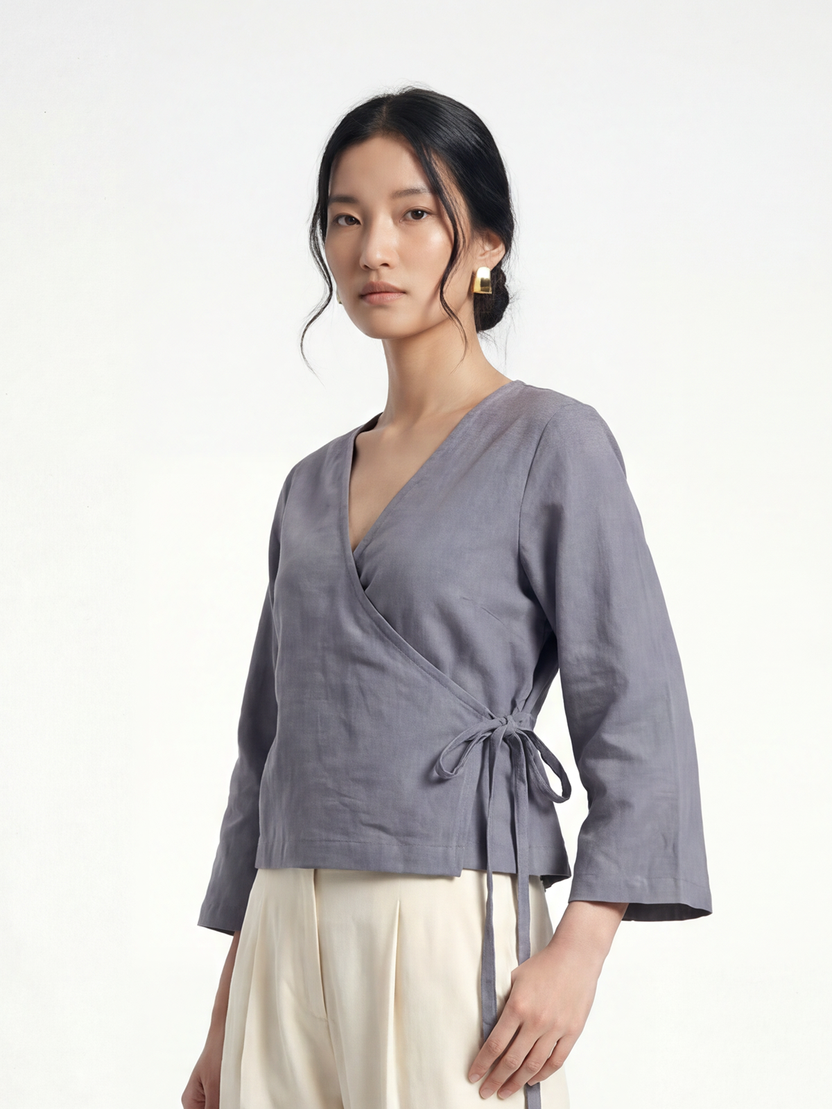 Female model wearing VUNN Slate Linen Wrap Top — slate-grey cropped linen wrap top with a deep V-neckline, side-tie closure and long flared sleeves